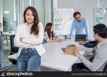Portrait of Asian Business woman with Arms Crossed and standing over the group of colleague partner when brainstorming meeting at modern workplace, human resource and small business owner concept