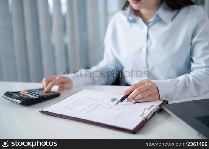 Portrait of Asian Business woman working from office taking reading and writing notes in note pad working on laptop computerin her workstation.