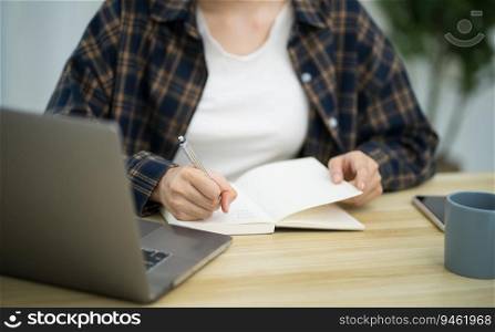 Portrait of  Asian Business woman working from office taking reading and writing notes in note pad working on laptop computer  in her workstation
