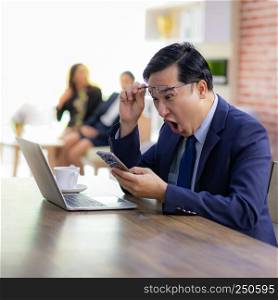 Portrait of Asian Businessman celebrate and glad for his success in cafe using smart phone and laptop with business team in background using for coporate background work, square composition