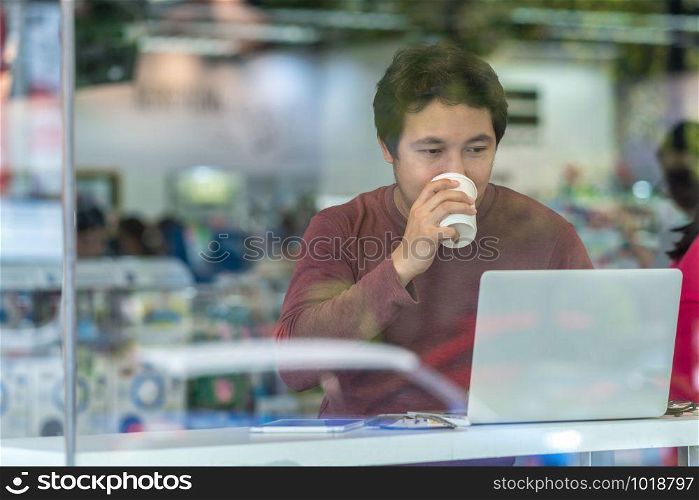 Portrait of asian businessman in casual suit drinking and using technology laptop for working in happiness action at the desk beside the glass in modern office,Business and lifestyle concept