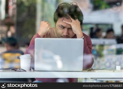 Portrait of asian businessman in casual suit using technology laptop for working in serious and exhausted action at the desk beside the glass in modern office,Business and lifestyle concept