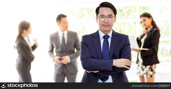 Portrait of asian businessman with business team in background at office window using for coporate working background, panoramic web banner composition