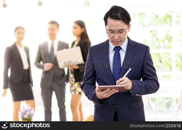 Portrait of asian businessman working using smart tablet with business team in background at office window using for coporate working background