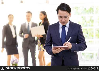 Portrait of asian businessman working using smart tablet with business team in background at office window using for coporate working background