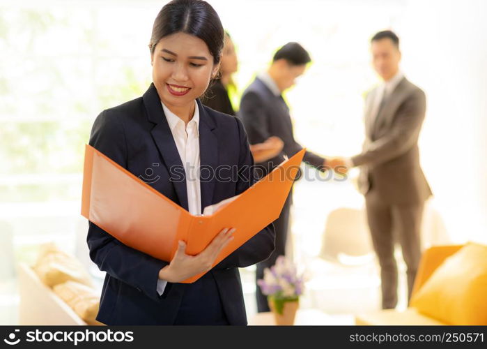 Portrait of Asian Businesswoman hold working file with business team in background using for coporate background work