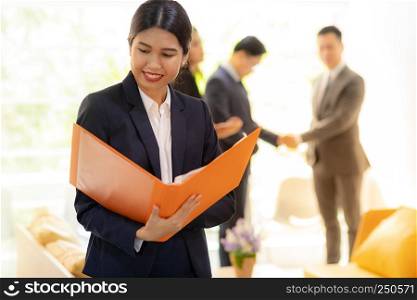 Portrait of Asian Businesswoman hold working file with business team in background using for coporate background work