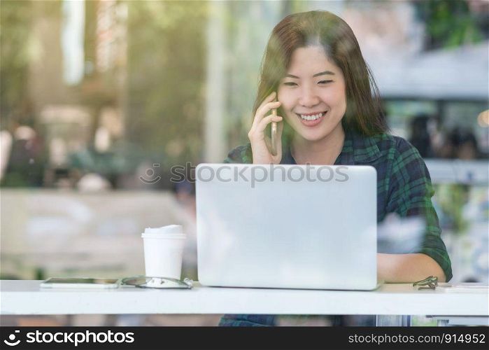 Portrait of asian businesswoman in casual suit talking and working with technology laptop in happiness action at the desk beside the glass in modern office, Business owner and entrepreneur concept