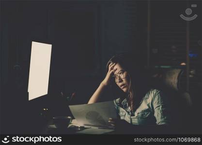 Portrait of Asian Businesswoman sitting and working hard on the table with front of computer desktop in workplace at late with serious action, Work hard and too late concept
