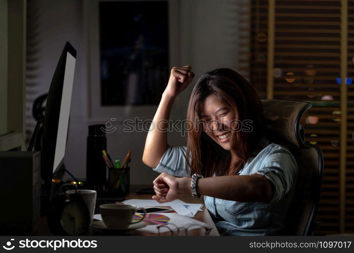 Portrait of Asian Businesswoman sitting and working hard with happiness action on the table with front of computer desktop in workplace at late time, Work hard and too late concept