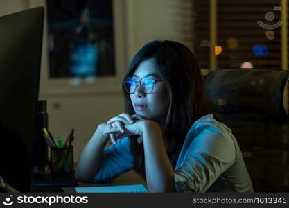 Portrait of Asian Businesswoman working hard and looking the digital graphic on the table with front of computer desktop in workplace at late with serious action, Work hard and too late concept