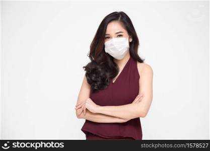 Portrait of Asian businesswomen in red dress with arms crossed and wearing protective medical mask for prevent virus Covid-19 and looking at camera isolated on white background