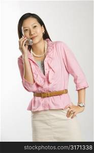 Portrait of Asian Chinese mid-adult female with hand on hip smiling and talking on cell phone.