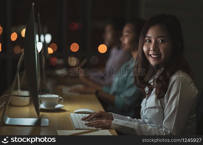 Portrait of Asian Female customer care service with business man smiling and working hard late in night shift at office,call center department,worker and overtime,teamwork with colleagues for success