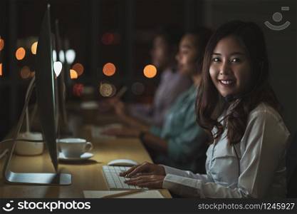 Portrait of Asian Female customer care service with business man smiling and working hard late in night shift at office,call center department,worker and overtime,teamwork with colleagues for success