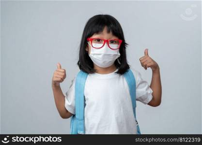 Portrait of Asian girl kid with protective face mask and school backpack and thumbs up, ready for new school year. Concept of kid going back to school and new normal lifestyle