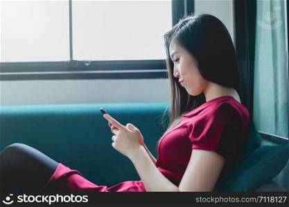 Portrait of Asian girl relaxing on a sofa at home texting on the smart phone in the living room at home