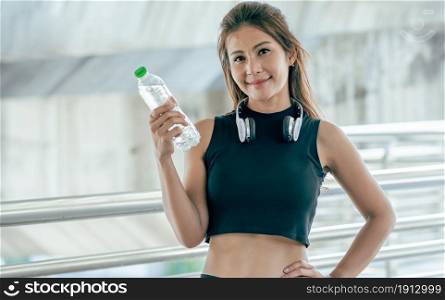 Portrait of Asian healthy and sportive woman wearing sport bra, smiling and holing bottle. Sport and Lifestyle Concept.