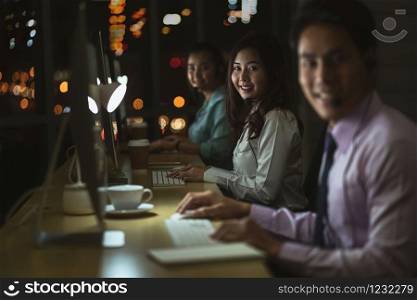 Portrait of Asian Male customer care service with businesswoman smiling and working hard late in night shift at office,call center department,worker and overtime,team work with colleagues for success