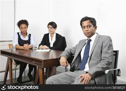 Portrait of Asian male with female colleagues in background at desk in office