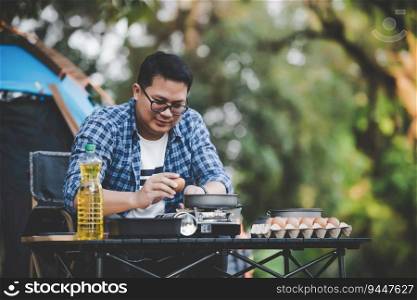 Portrait of Asian man glasses breaking egg at the c&site. Outdoor cooking, traveling, c&ing, lifestyle concept.