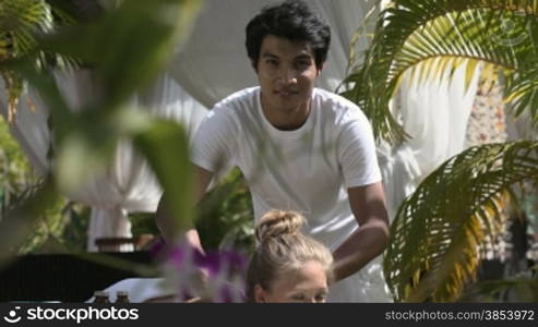 Portrait of asian masseur giving massage to young beautiful blonde caucasian woman during beauty treatment in luxury spa