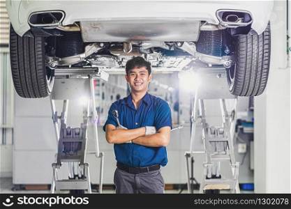 Portrait of Asian mechanic with repair equipment standing under the car in maintainance service center which is a part of showroom, technician or engineer professional work for customer