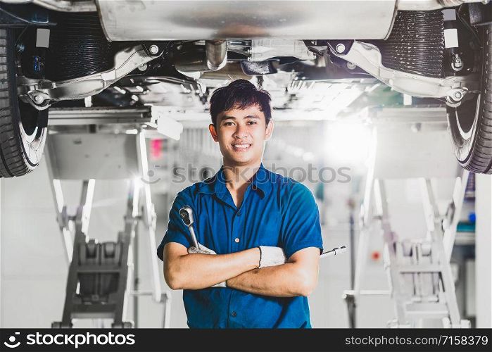 Portrait of Asian mechanic with repair equipment standing under the car in maintenance service center which is a part of showroom, technician or engineer professional work for customer