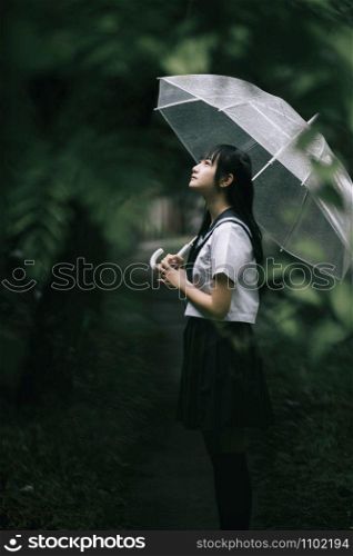 Portrait of Asian school girl walking with umbrella at nature walkway on raining