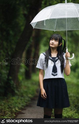 Portrait of Asian school girl walking with umbrella at nature walkway on raining
