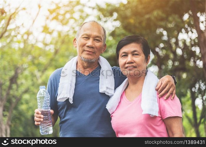 Portrait of Asian Senior couple in blue and pink shirt smiling and standing before exercising at park outdoor. Good health.