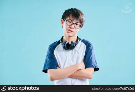 Portrait of Asian teenage boy in studio with light blue background . Music headphone concept .