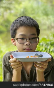 Portrait of Asian Thai pensive boy looks at fish bone of white perch fish fried eaten clearly on plate