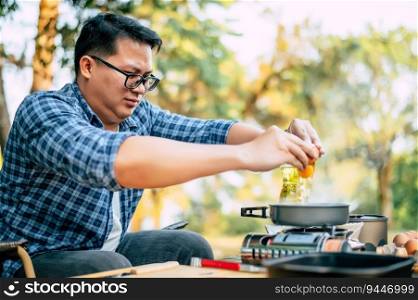 Portrait of Asian traveler man glasses frying a tasty fried egg in a hot pan at the campsite. Outdoor cooking, traveling, camping, lifestyle concept.