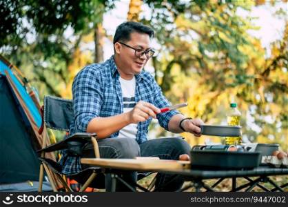 Portrait of Asian traveler man glasses frying a tasty fried egg in a hot pan at the c&site. Outdoor cooking, traveling, c&ing, lifestyle concept.