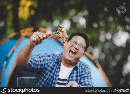 Portrait of Asian traveler man glasses pork steak frying, BBQ in roasting skillet pan or pot at a c&site. Outdoor cooking, traveling, c&ing, lifestyle concept.