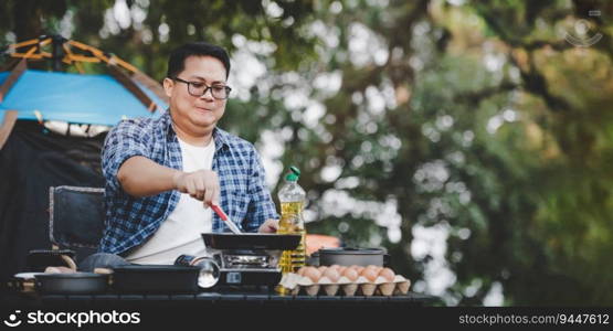 Portrait of Asian traveler man glasses pork steak frying, BBQ in roasting skillet pan or pot at a c&site. Outdoor cooking, traveling, c&ing, lifestyle concept.