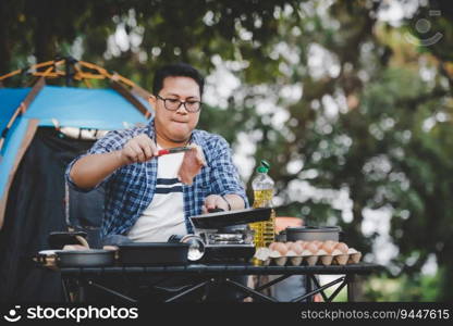 Portrait of Asian traveler man glasses pork steak frying, BBQ in roasting skillet pan or pot at a c&site. Outdoor cooking, traveling, c&ing, lifestyle concept.