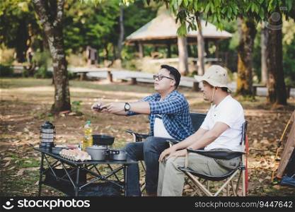 Portrait of Asian traveler men taking a photo on smartphone at a c&site. Outdoor cooking, traveling, c&ing, lifestyle concept.