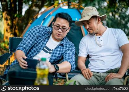 Portrait of Asian traveler men taking a photo on smartphone at a campsite. Outdoor cooking, traveling, camping, lifestyle concept.