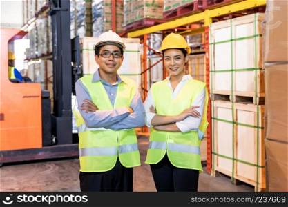 Portrait of Asian warehouse manager and worker arm crossed with warehouse worker operate forklift to check inventory in background. Reopening business warehouse technology and logistic concept.