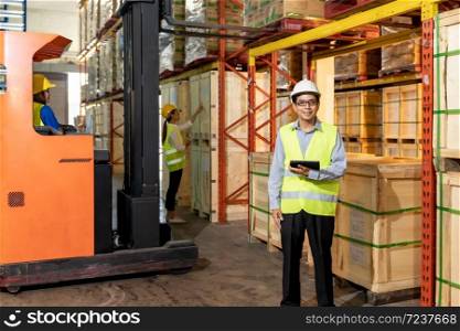 Portrait of Asian warehouse manager hold digital tablet with warehouse worker operate forklift to check inventory in background. Reopening business warehouse technology and logistic concept.