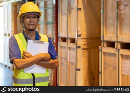 Portrait of Asian warehouse worker with clipboard job cross arm in large distribution warehouse background. Reopening business warehouse inventory and logistic concept.