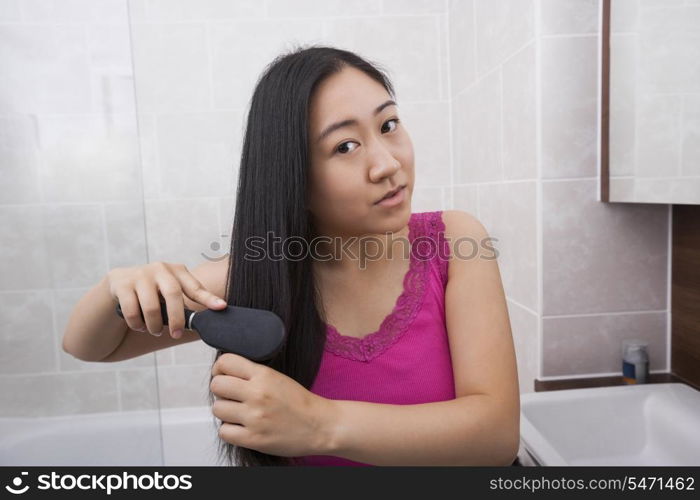 Portrait of Asian woman brushing her hair in bathroom