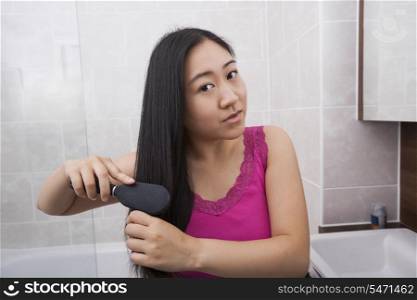 Portrait of Asian woman brushing her hair in bathroom