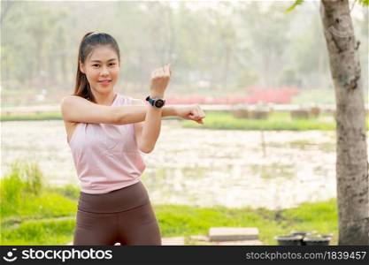 Portrait of Asian woman do arm stretching in park or garden with lake or flower field as background and morning light.