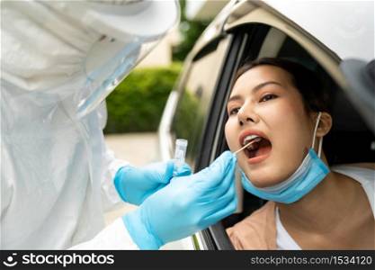 Portrait of asian woman drive thru coronavirus covid-19 test by medical staff with PPE suit by throat swab. New normal healthcare drive thru service and medical concept.