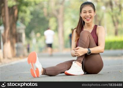 Portrait of Asian woman look at camera and sit with one&rsquo;s knees up on road of green park or garden with morning light.