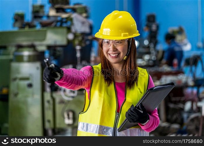 Portrait of Asian woman sales engineer checking the job list in paper over the photo blurred of lathe and milling machine background in metal factory, business industry with safety concept