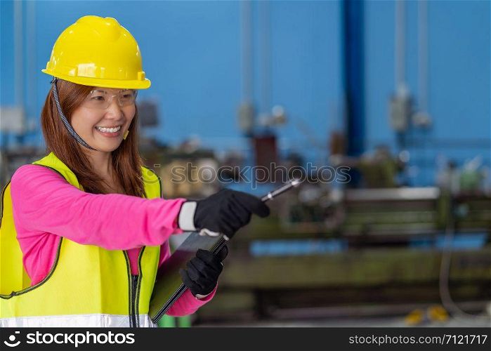 Portrait of Asian woman sales engineer checking the job list in paper over the photo blurred of lathe and milling machine background in metal factory, business industry concept